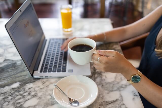 A woman's hands holding a coffee cup and typing on a laptop