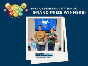 A woman holding a basket of prizes and a boy is holding three glass bottles of Coke-a-cola. More prizes can be seen on a table behind the two people. Graphic text reads, "2024 Cybersecurity Bingo Grand Prize Winners!"