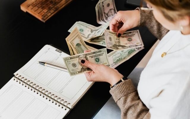 Woman sitting at desk with dollar bills of various amounts scattered around her.