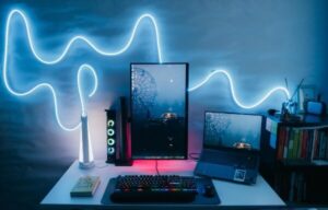 Windows 11 computer setup on desk in a dark room. A neon light in a blue, squiggly line lights up the background.