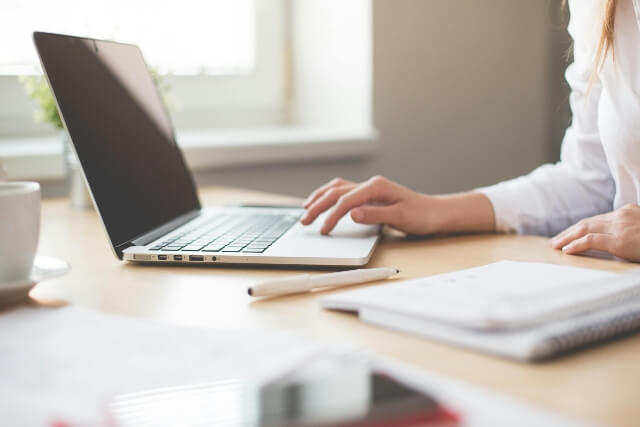 Woman sitting at a desk working on a laptop. A notebook can be seen in the foreground.